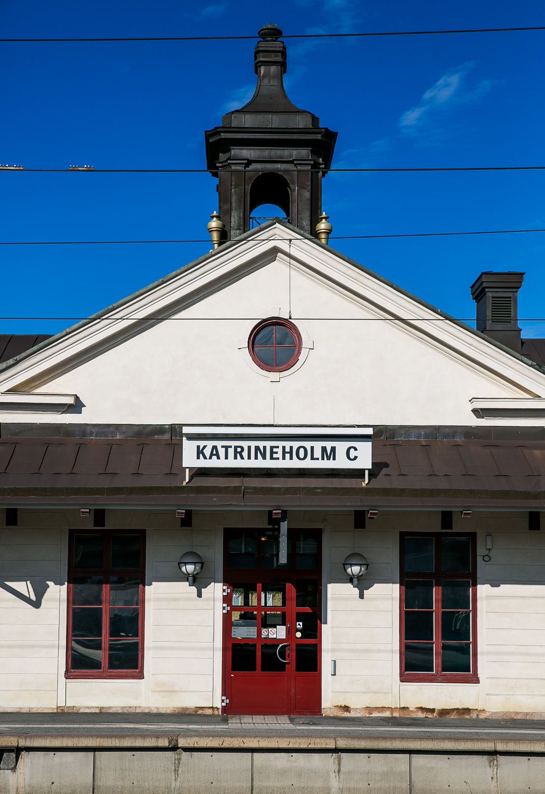 White train station building with red trim and Katrineholm sign against blue sky.