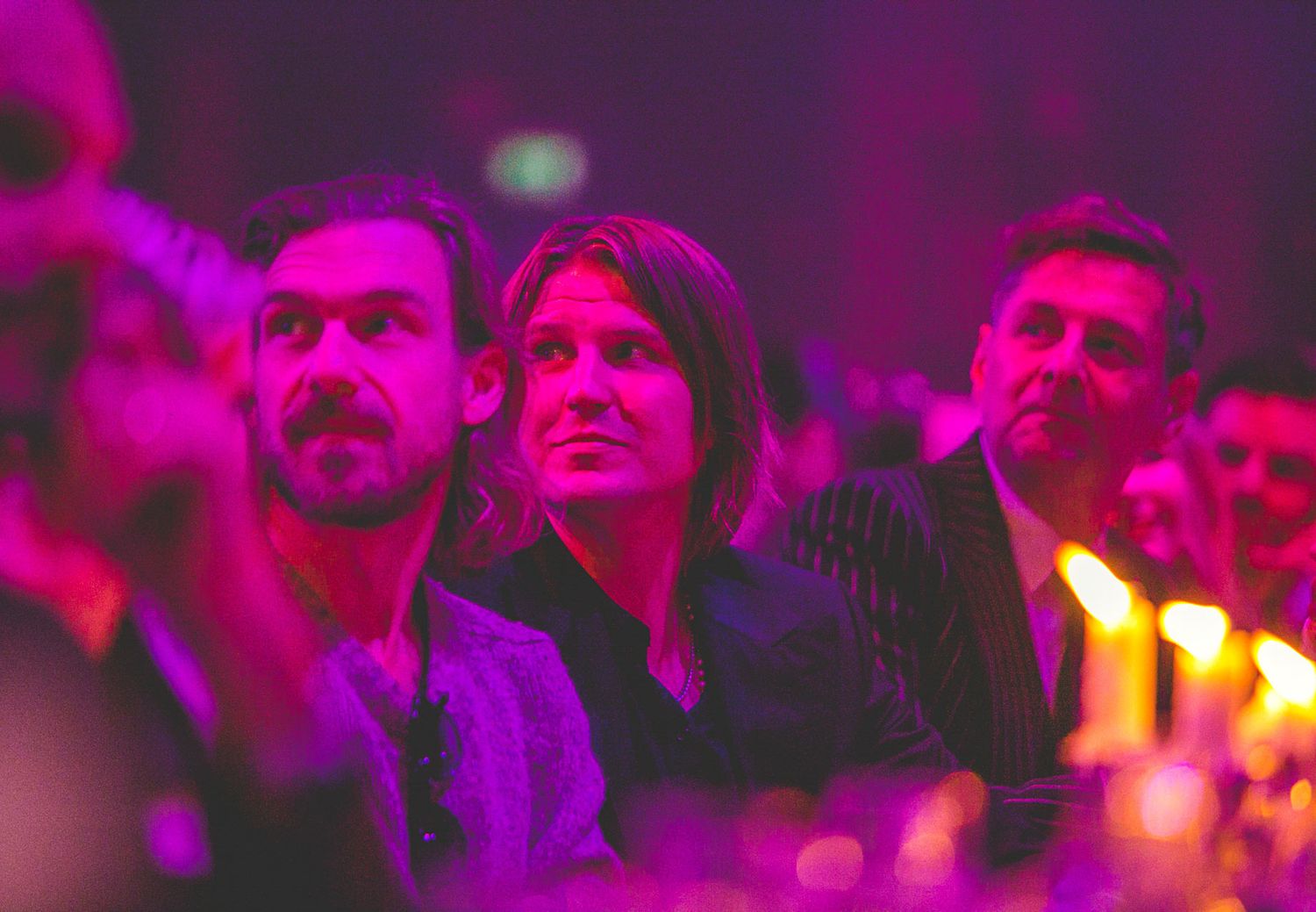 Crowd silhouettes under vibrant purple and pink stage lighting.