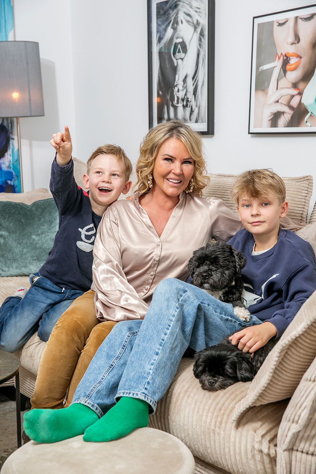 Familj kopplar av i en beige soffa med en svart hund och inramade konstverk i bakgrunden