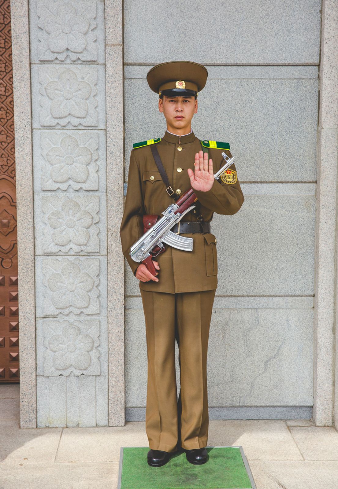 Military guards in brown uniforms standing at attention outside a stone building.