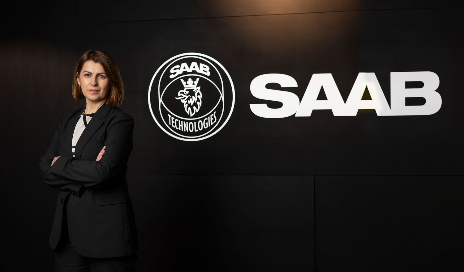 Företagsprofilbild med SAAB-logotyp och figur i formell klädsel mot mörk bakgrund