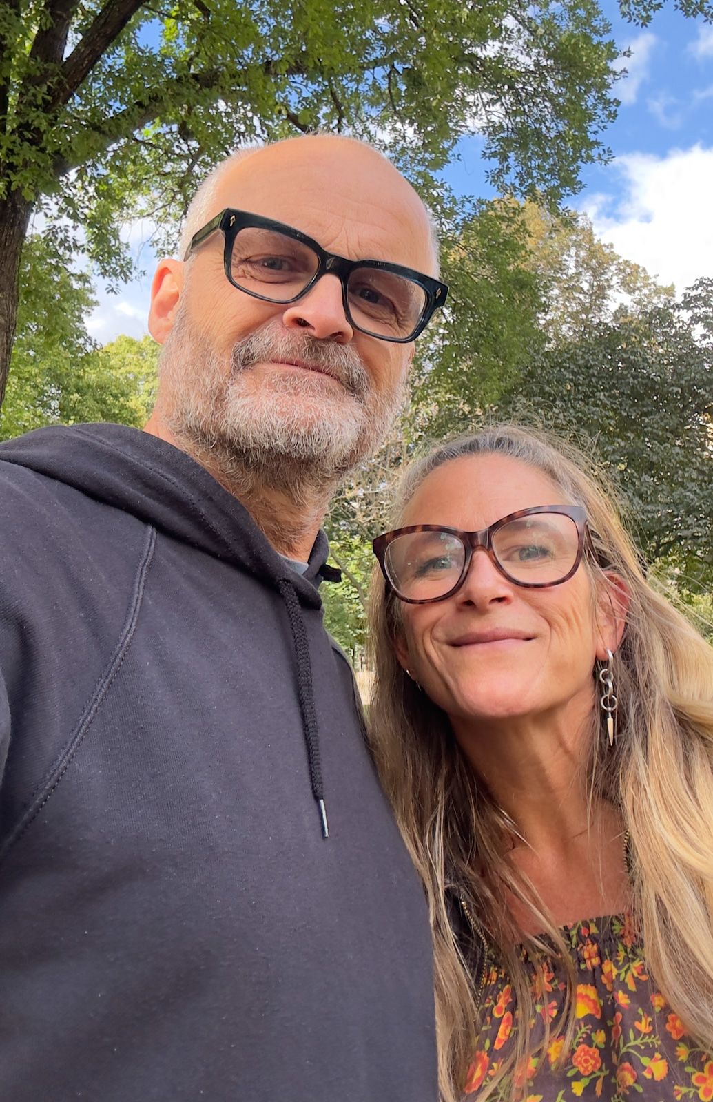 Två personer tar selfies tillsammans utomhus på en solig dag med träd i bakgrunden
