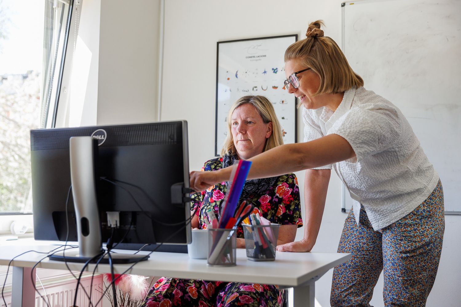 People working together at a desk with a Dell computer monitor in a bright office space.