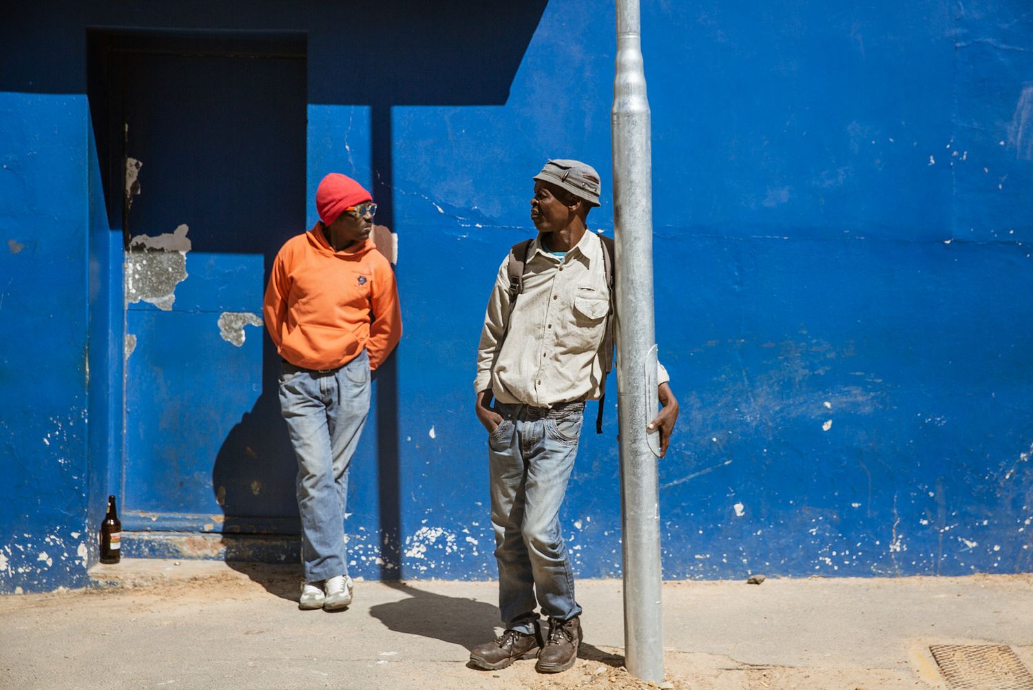 People sitting against a bright blue wall in an outdoor setting.