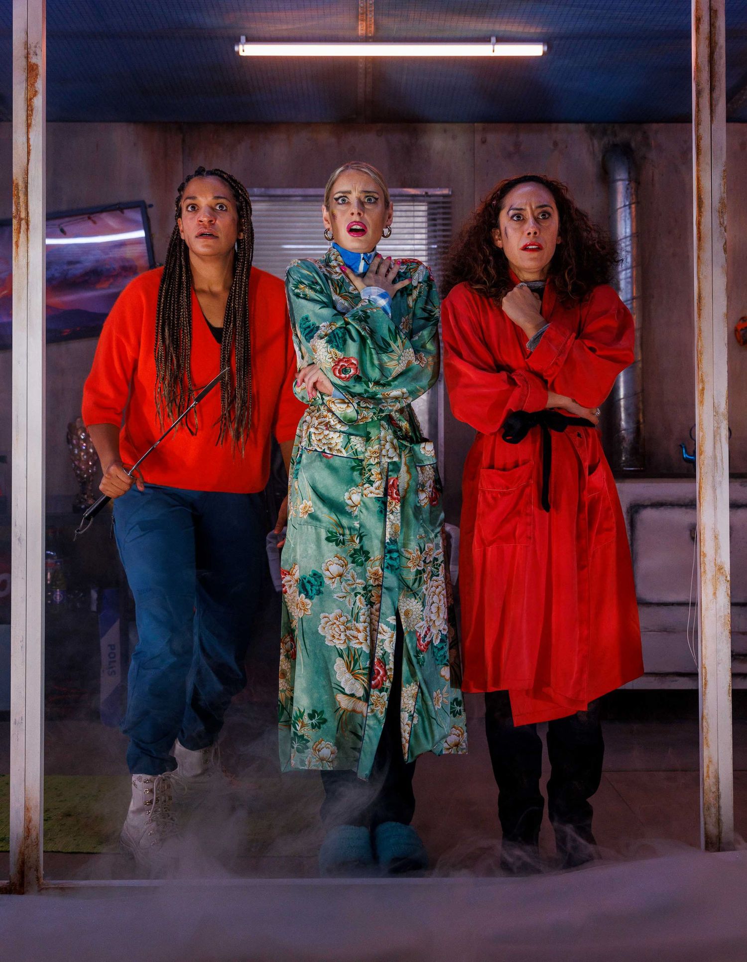 Performers in red and teal dresses posing theatrically under fluorescent lighting.