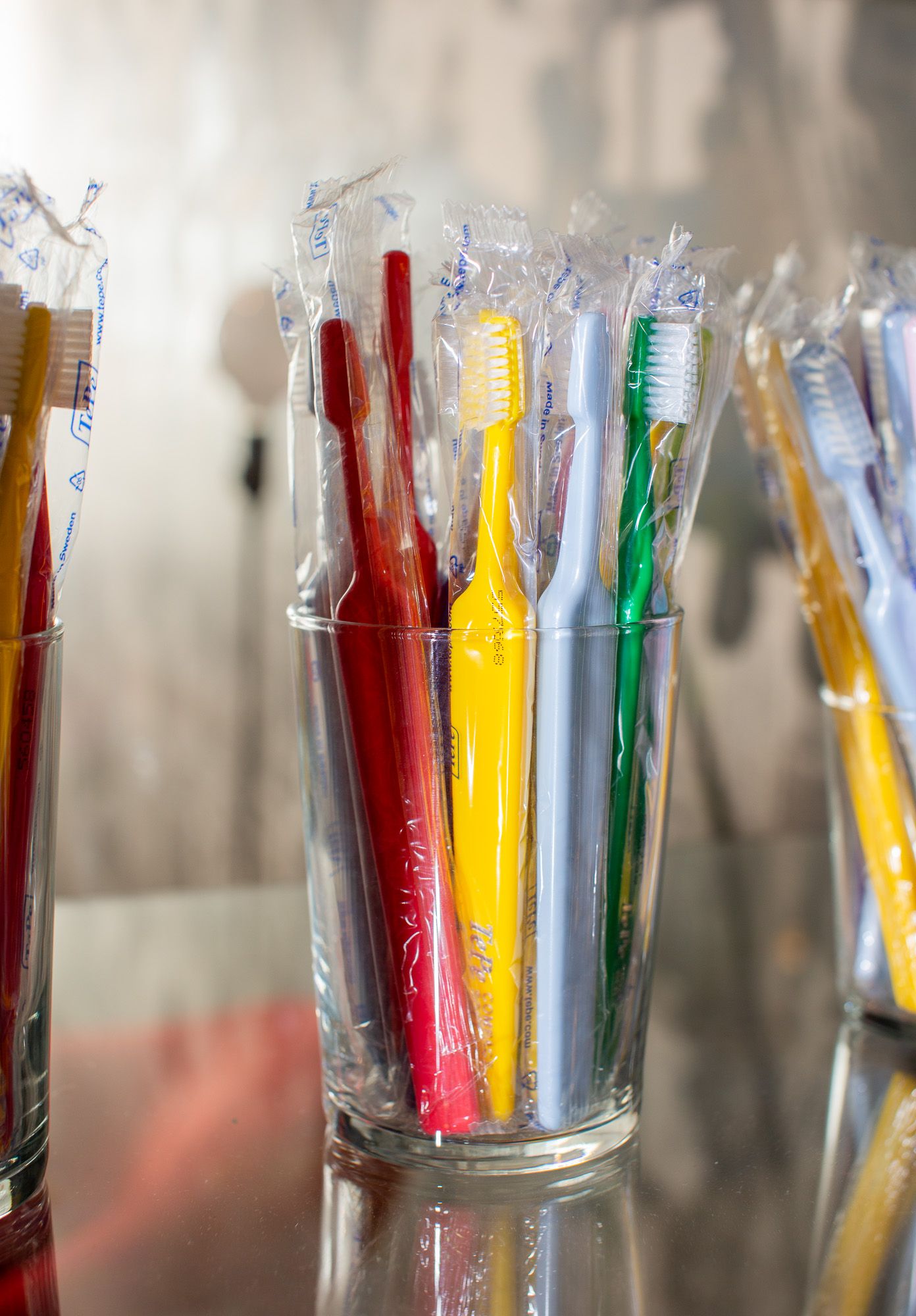 Colorful toothbrushes individually wrapped in plastic displayed in clear glass container.