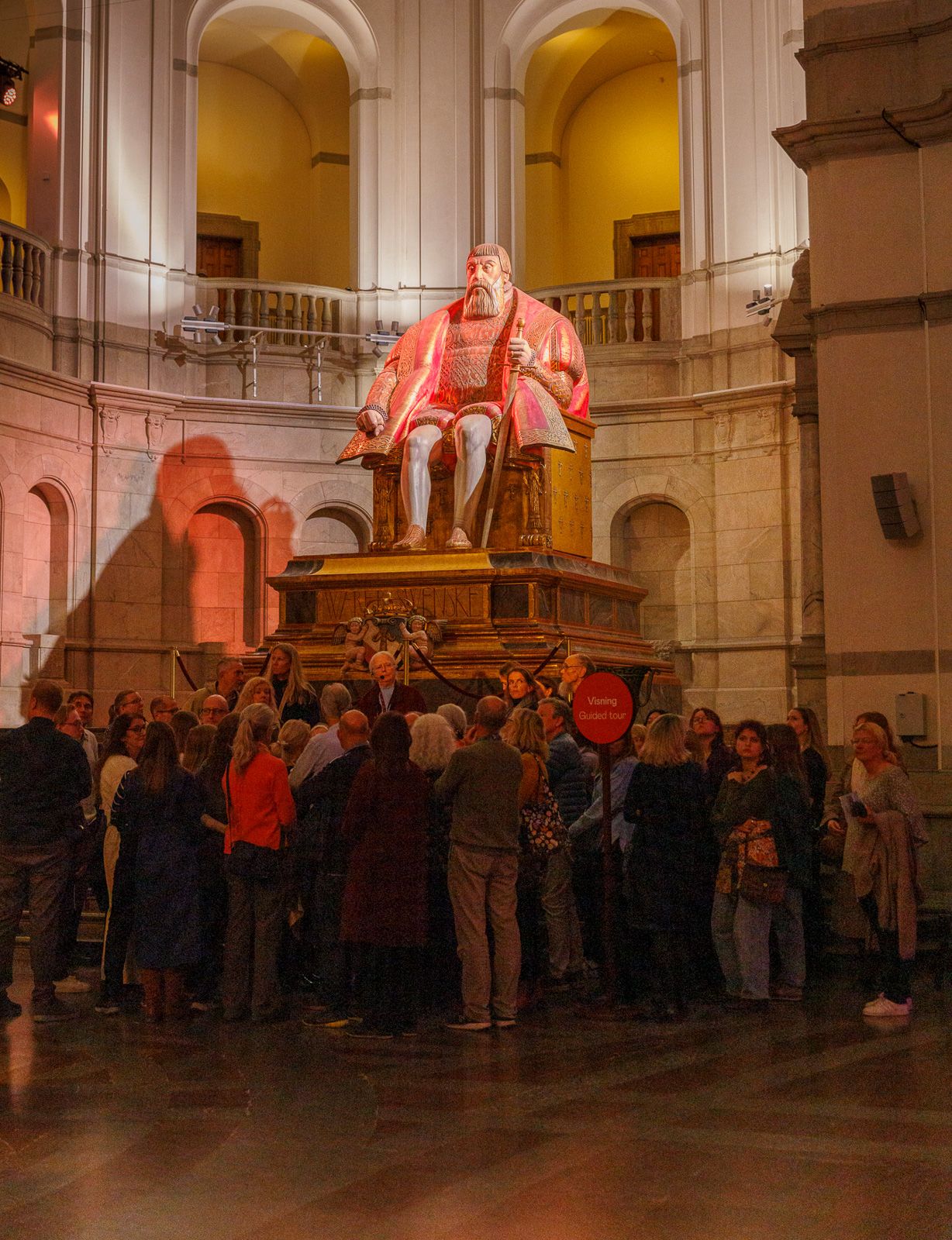 Large crowd gathered in an ornate hall with warm lighting and architectural details.