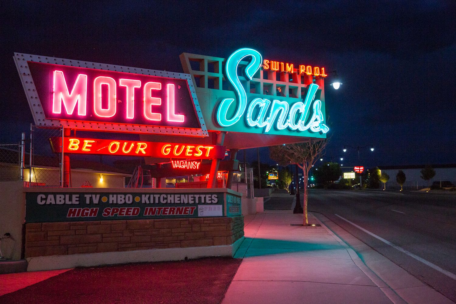 Vintage neon motel signs glowing pink and blue at night along a desert highway.
