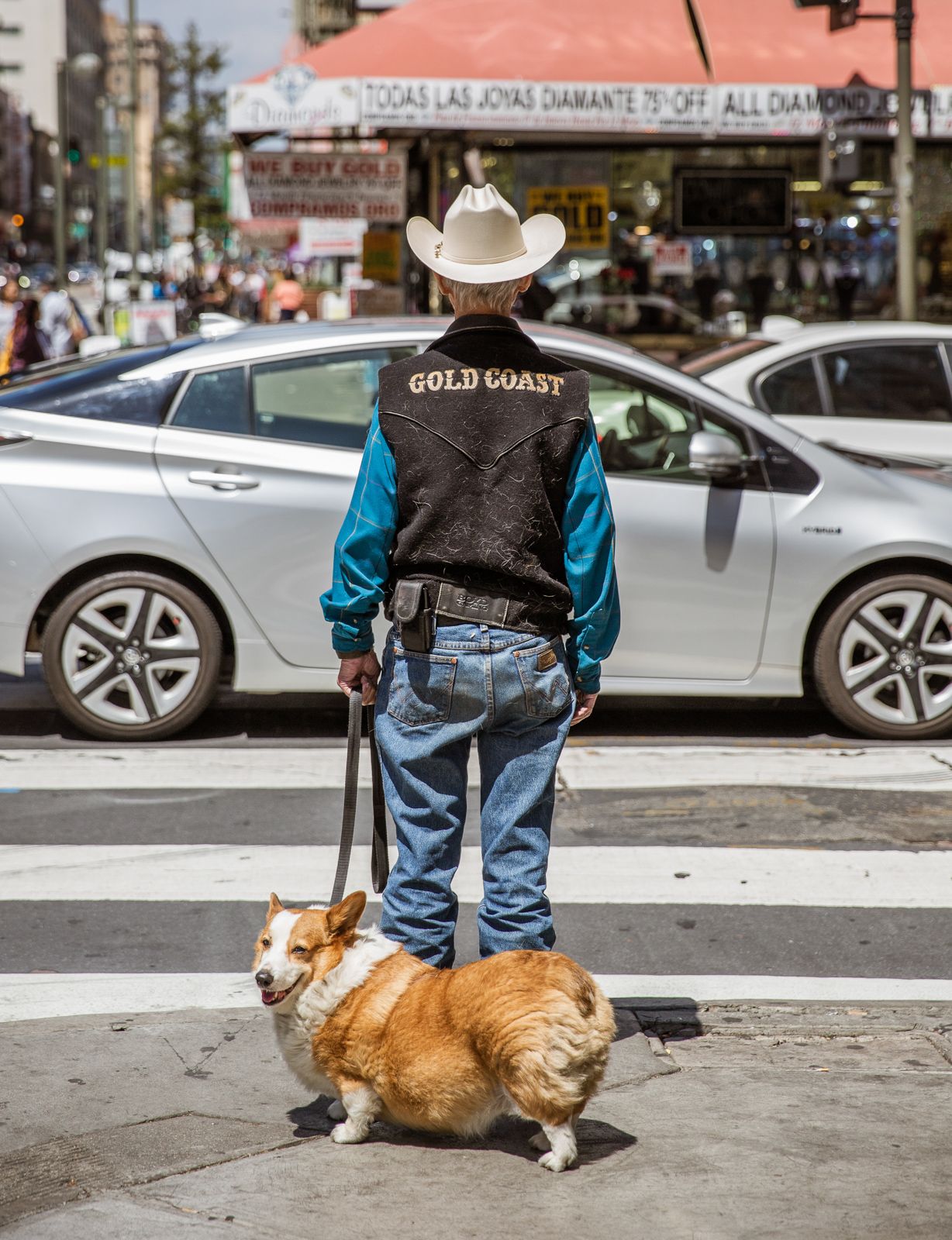 Corgi dog resting on sidewalk next to person in denim and western wear.