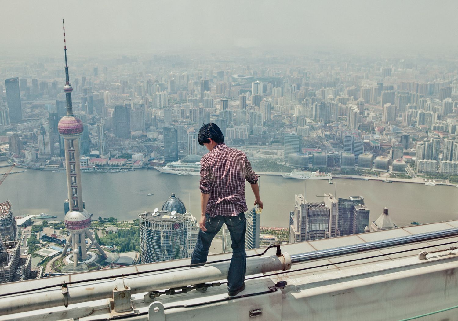 Person walking along the edge of a high-rise building with cityscape views below.