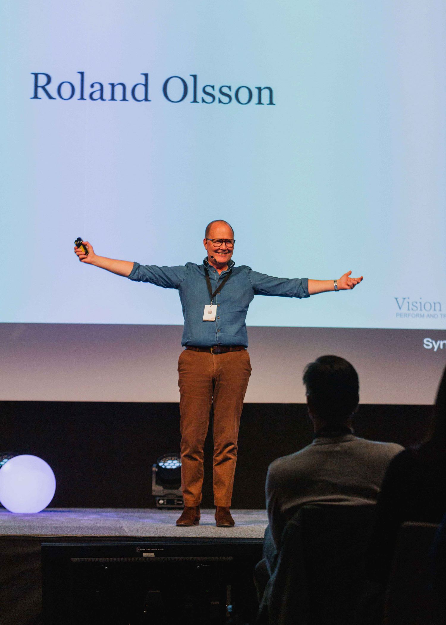 Talarpresentation på scen med projektionsskärm i bakgrunden