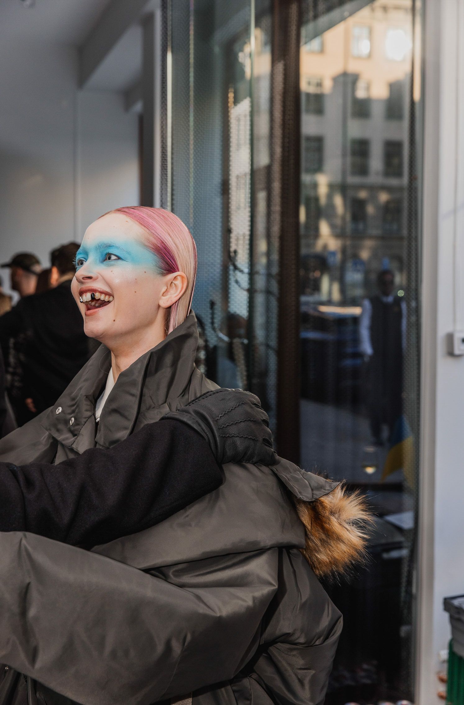 Person in dark jacket leaning back dramatically against window with colored lighting.
