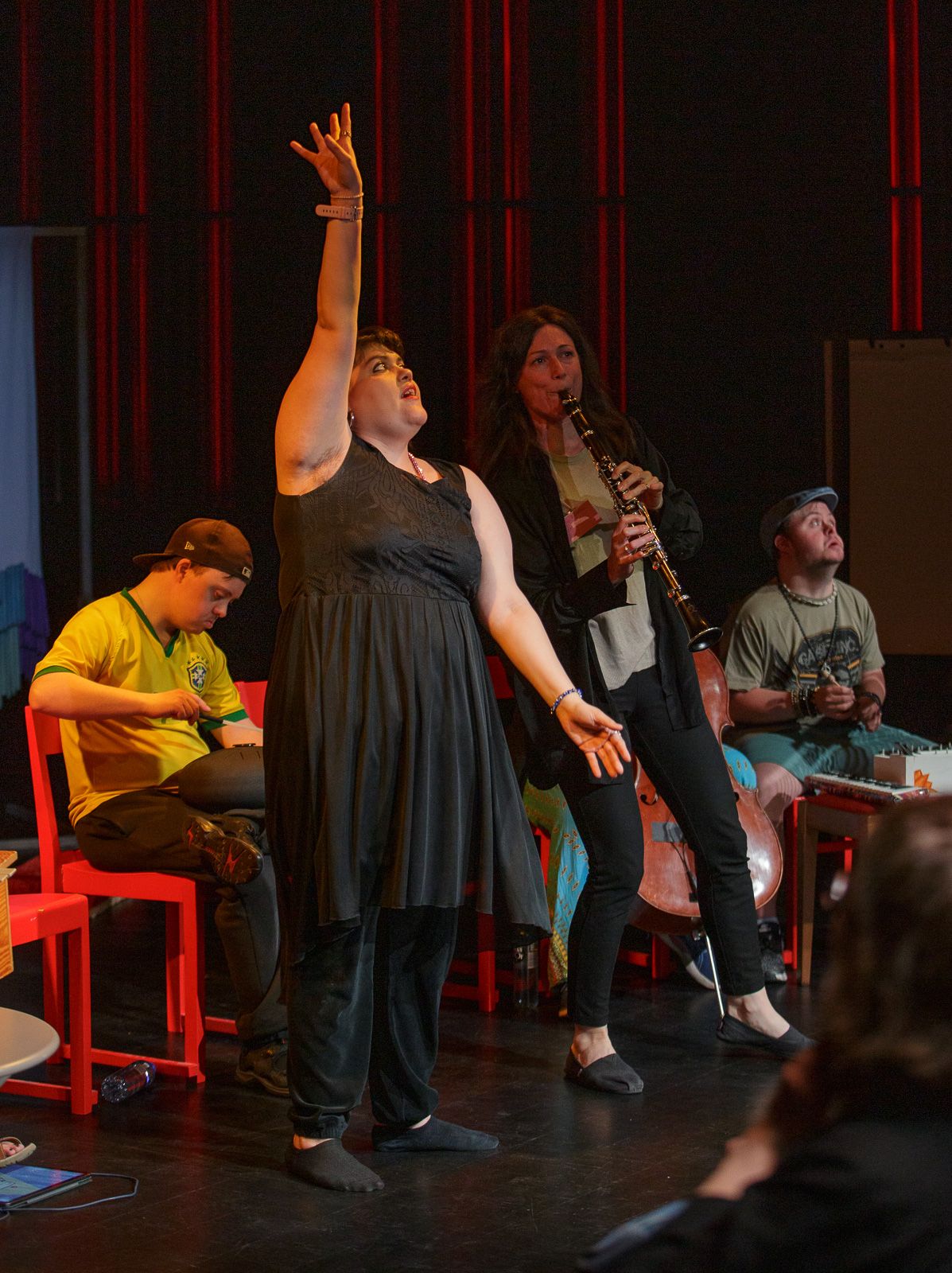 Performers engage in an expressive stage production with dramatic red lighting.