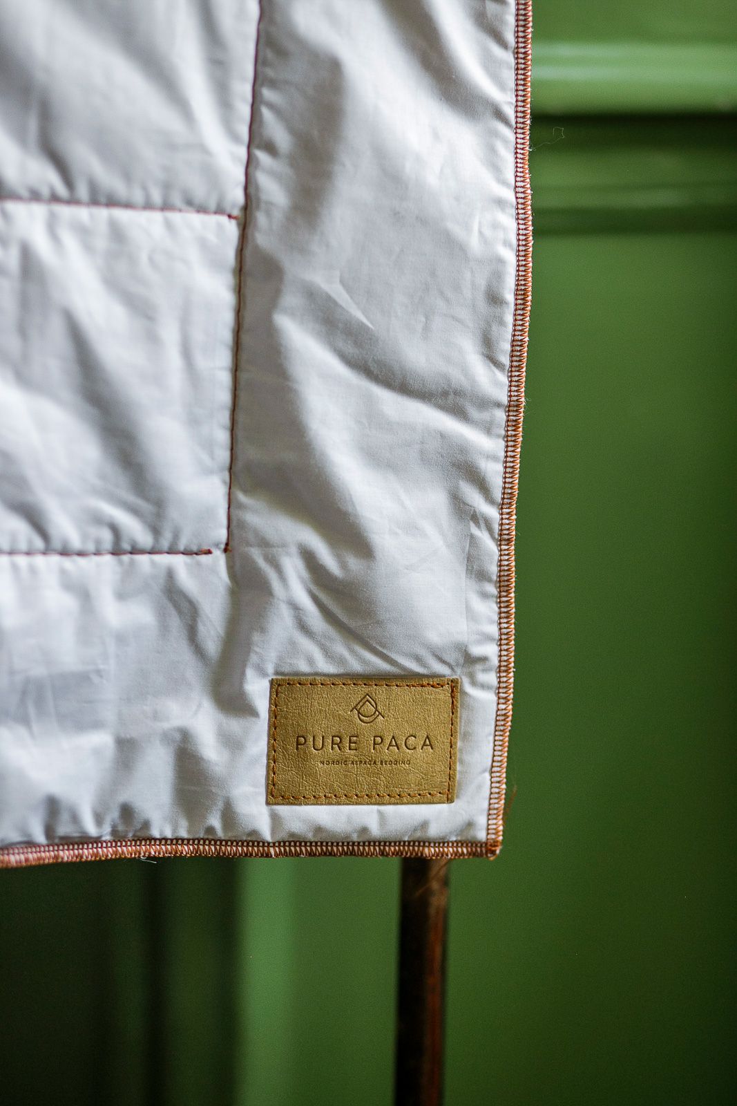 Close-up detail of white fabric with Pure Paca leather label against green background.