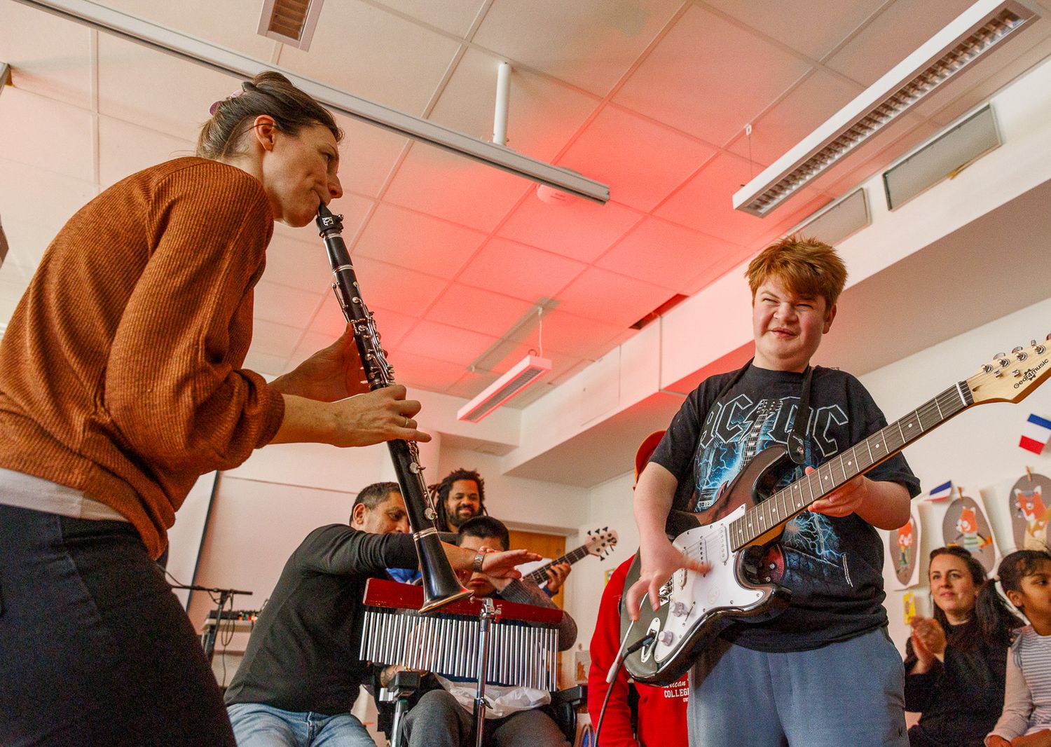 Musicians play instruments during a performance session in a room with red lighting.