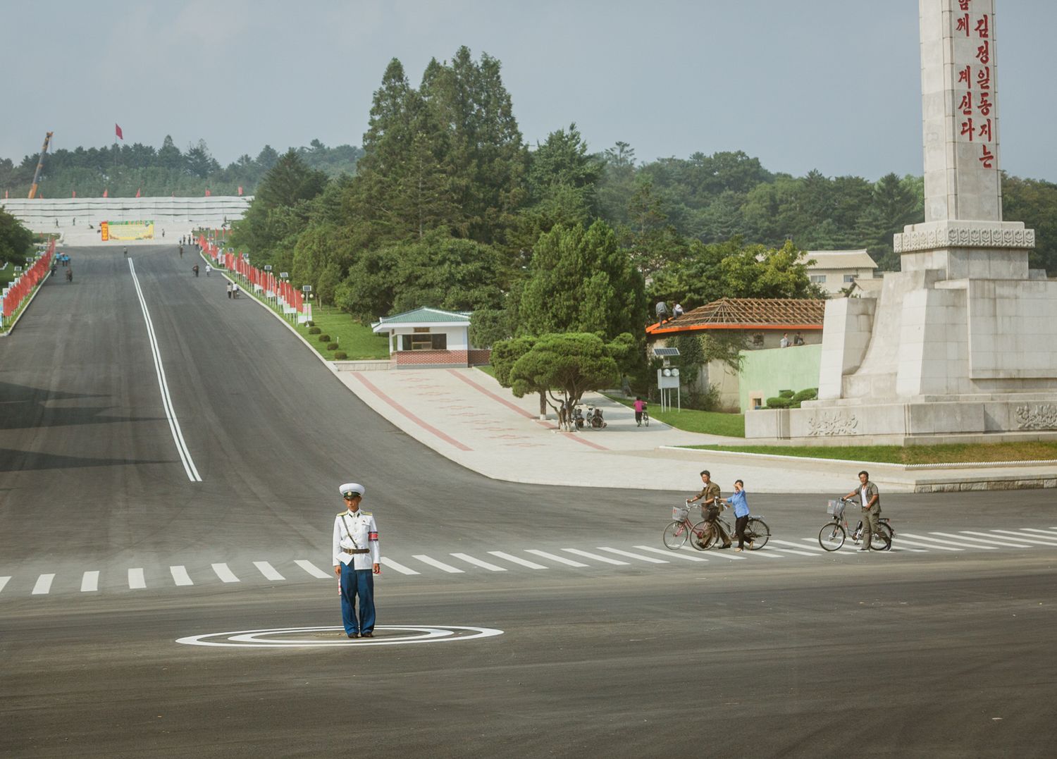 Empty wide roads and intersections in North Korea with occasional cyclists and pedestrians visible.