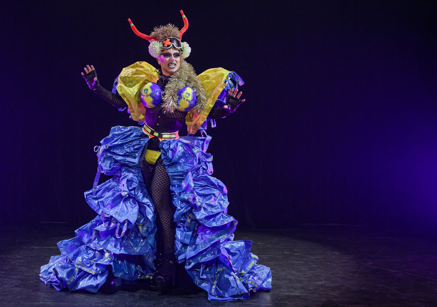 Dancers in ruffled blue dresses perform on a dark stage with dramatic lighting.
