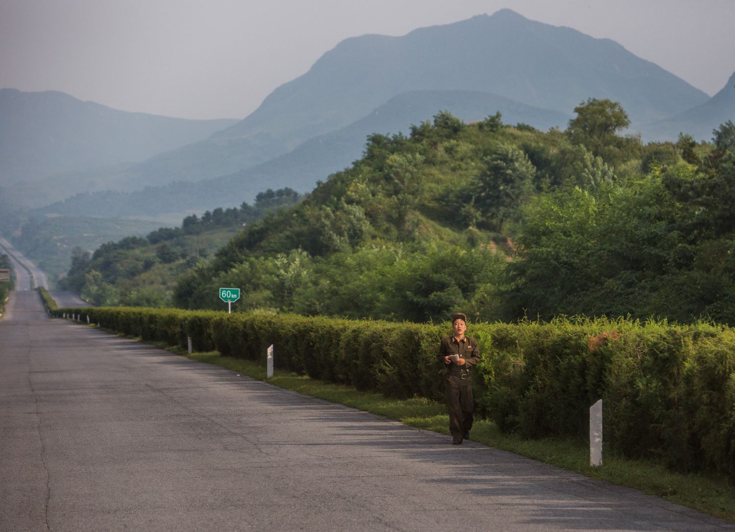 Misty mountain road stretches into the distance with green vegetation on both sides.