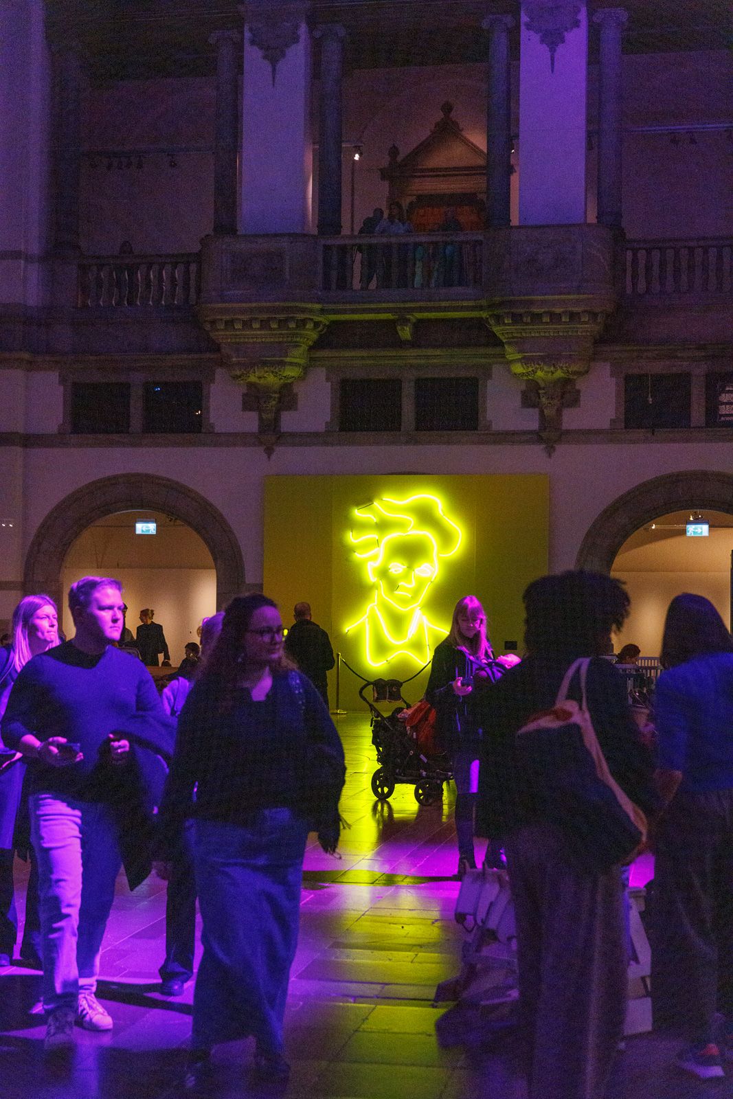 People mingling in a grand hall with purple and yellow lighting effects.
