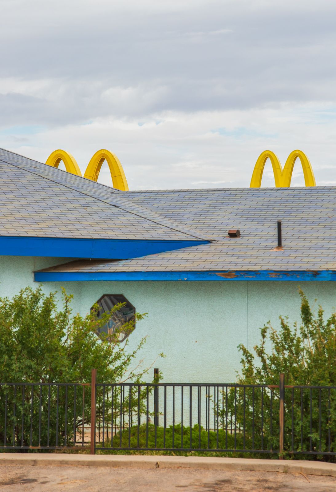 McDonald's restaurant exterior with blue roof trim and landscaping against cloudy sky.