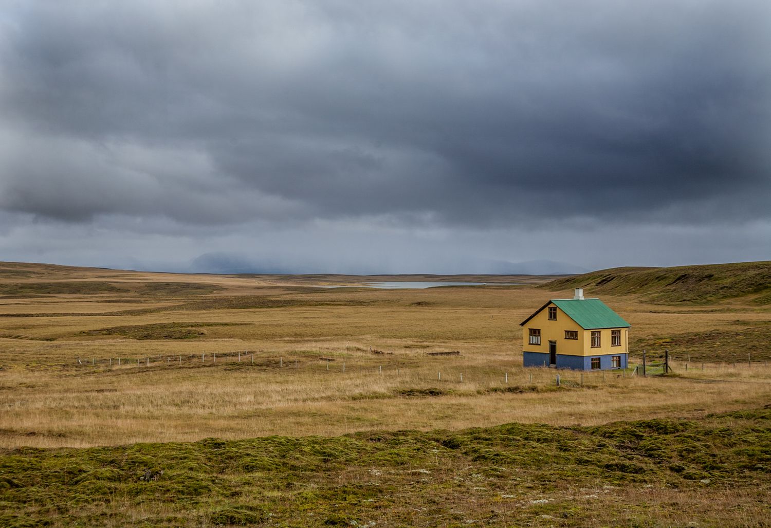 Panoramic landscape of remote houses on barren grassland under stormy skies.