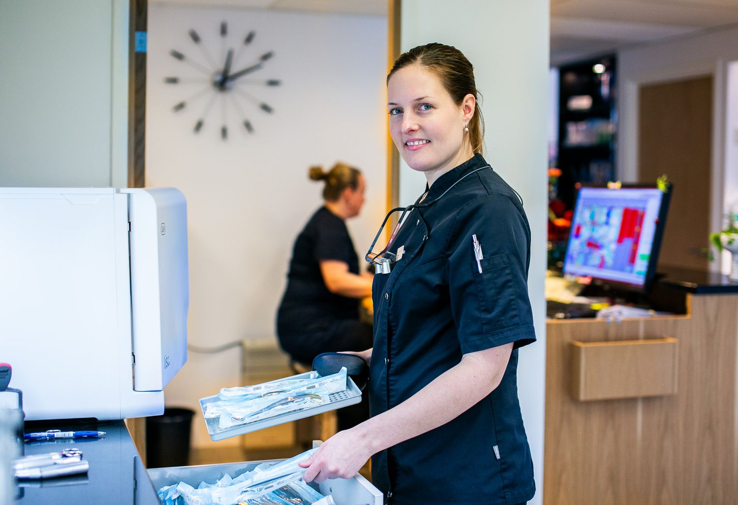 Healthcare worker in dark uniform working at reception desk with office equipment.