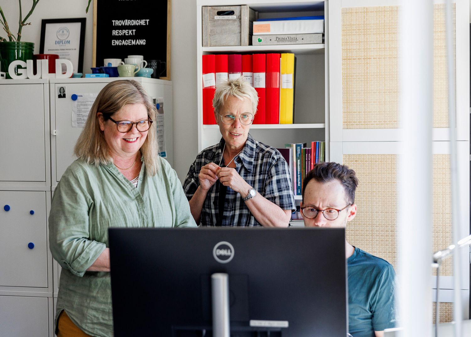 Two people collaborating at a desk while looking at a computer monitor in an office setting.