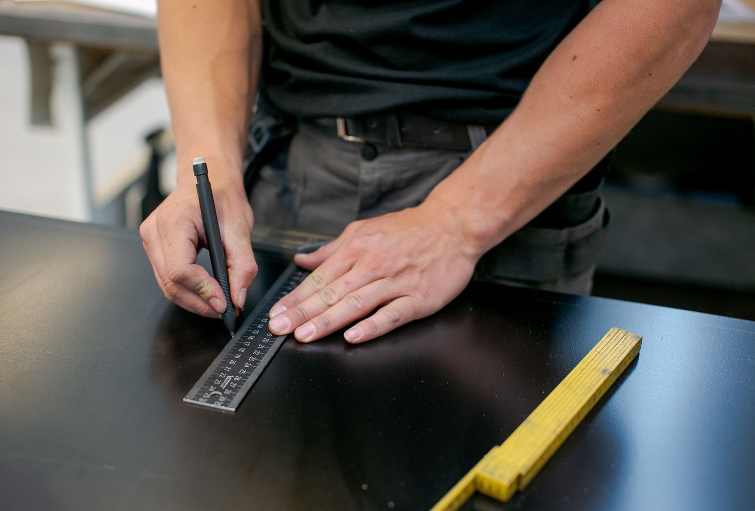 Close-up of hands using measuring tools on dark surface in workshop setting.