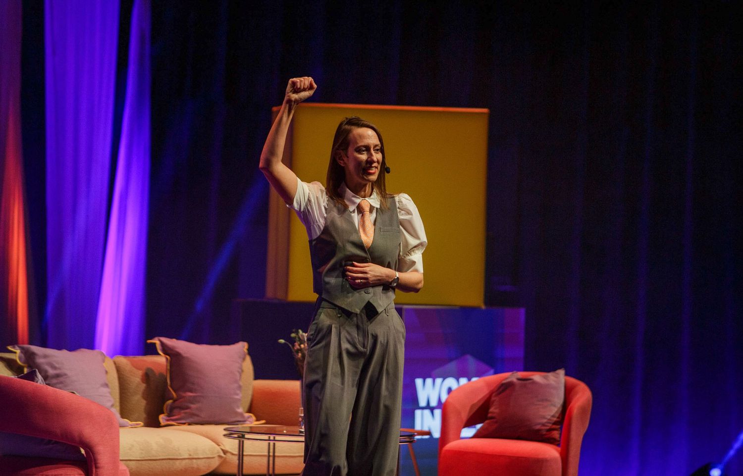 Stage setup at Women in Tech conference with purple lighting and presentation screens.