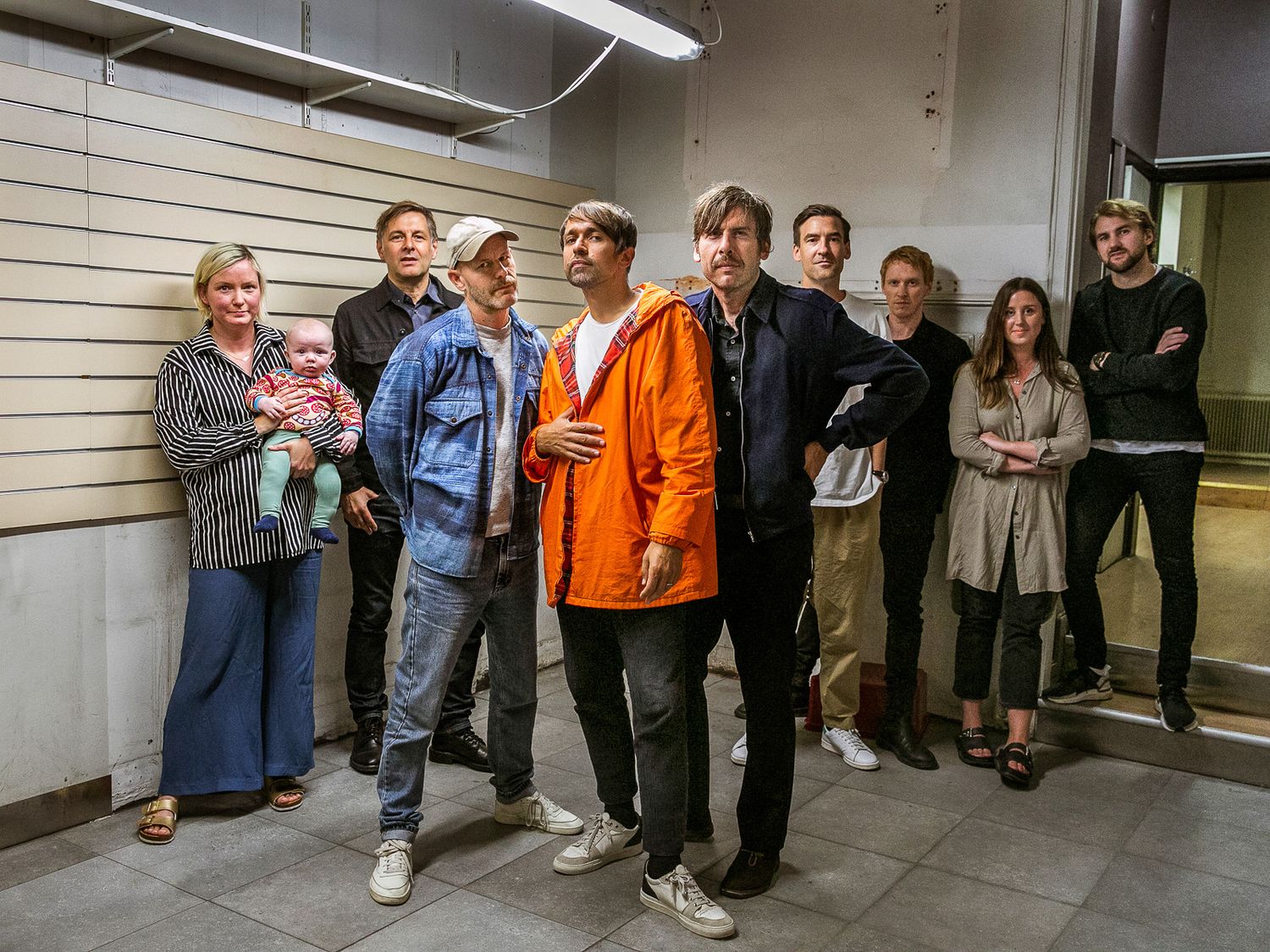 Large group gathered along a white wall in an institutional setting.