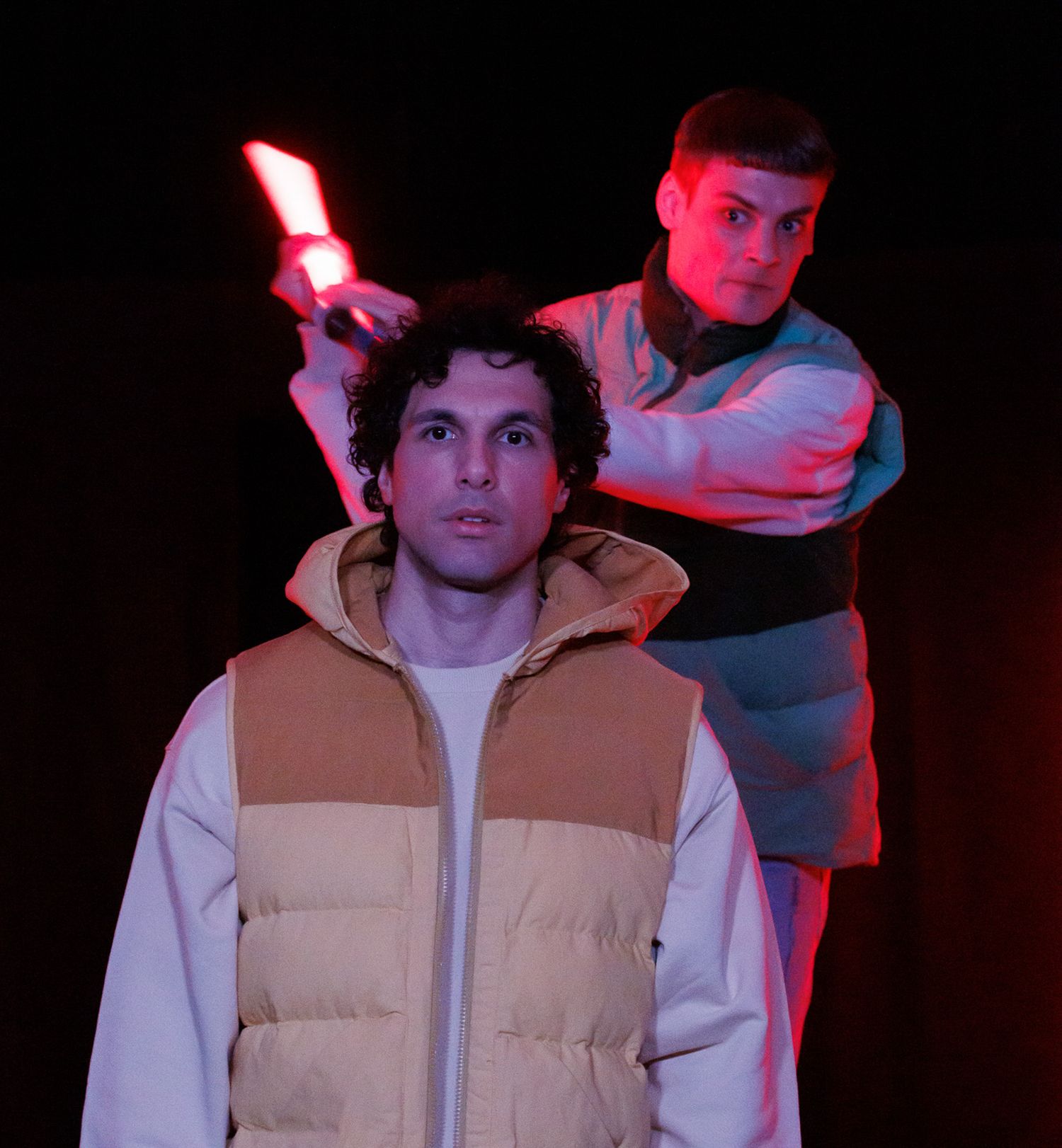 Two performers in casual wear posing dramatically with red lighting effects.