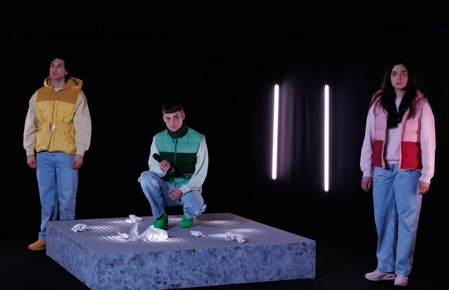 People in colorful casual wear stand on stage with vertical light bars in background.