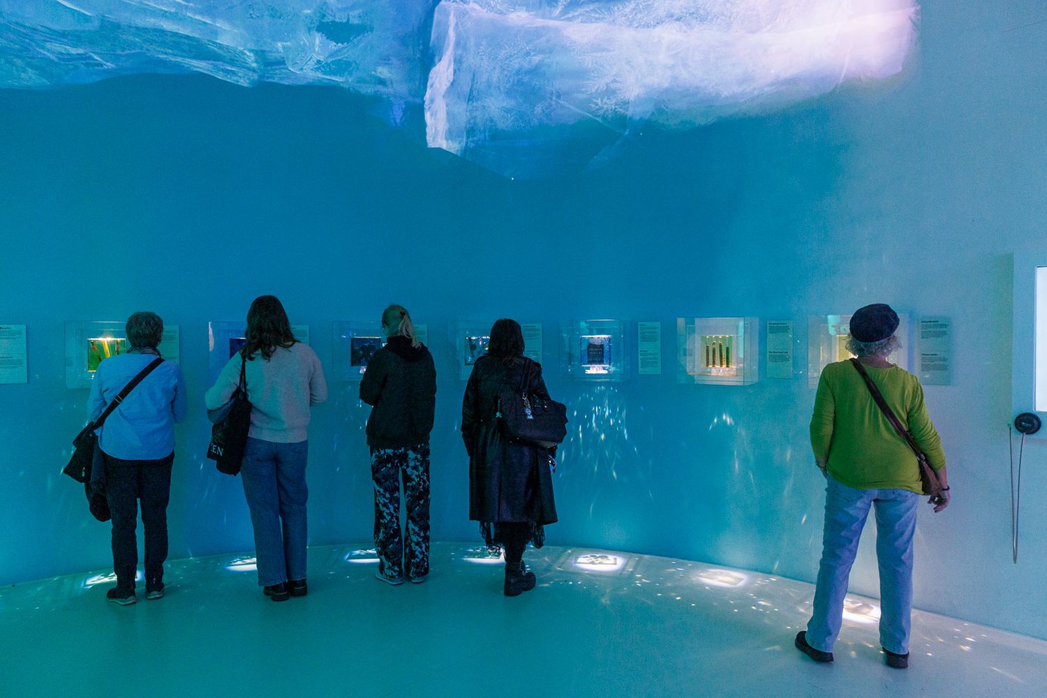 People viewing art installations in a blue-lit gallery space.