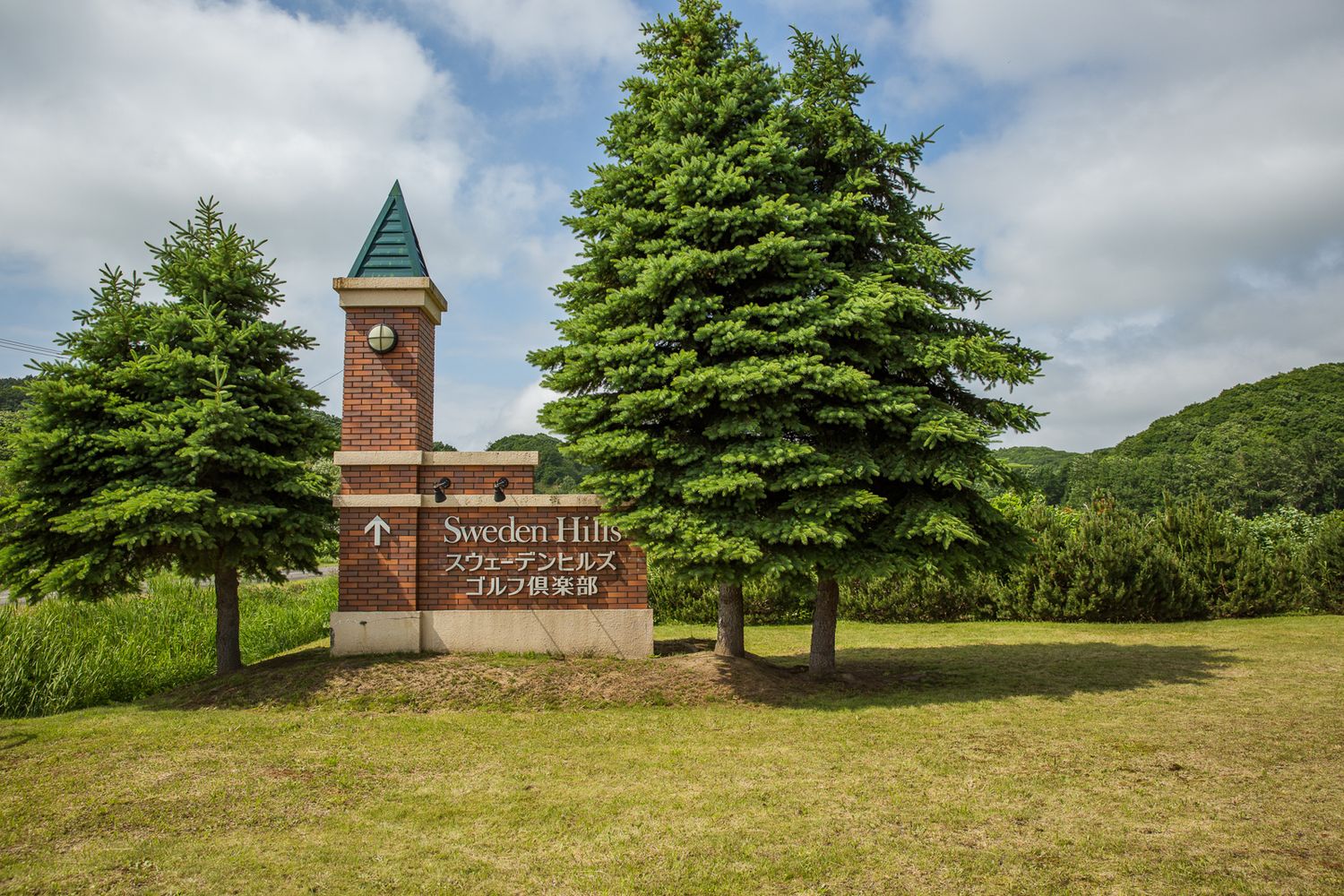 Panoramic view of a hilltop church with green trees and cloudy sky.