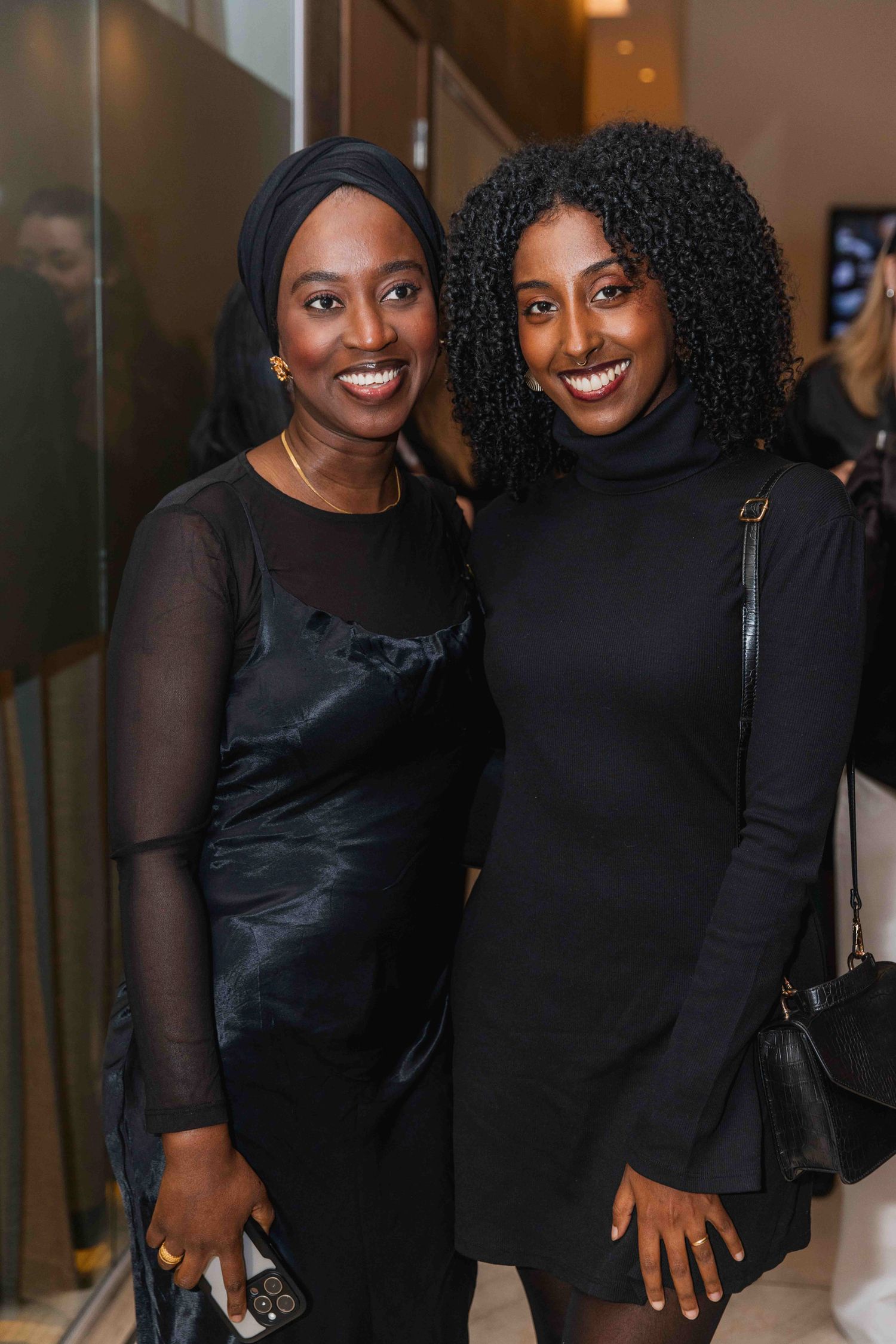 Two women in matching black outfits posing together at an event.