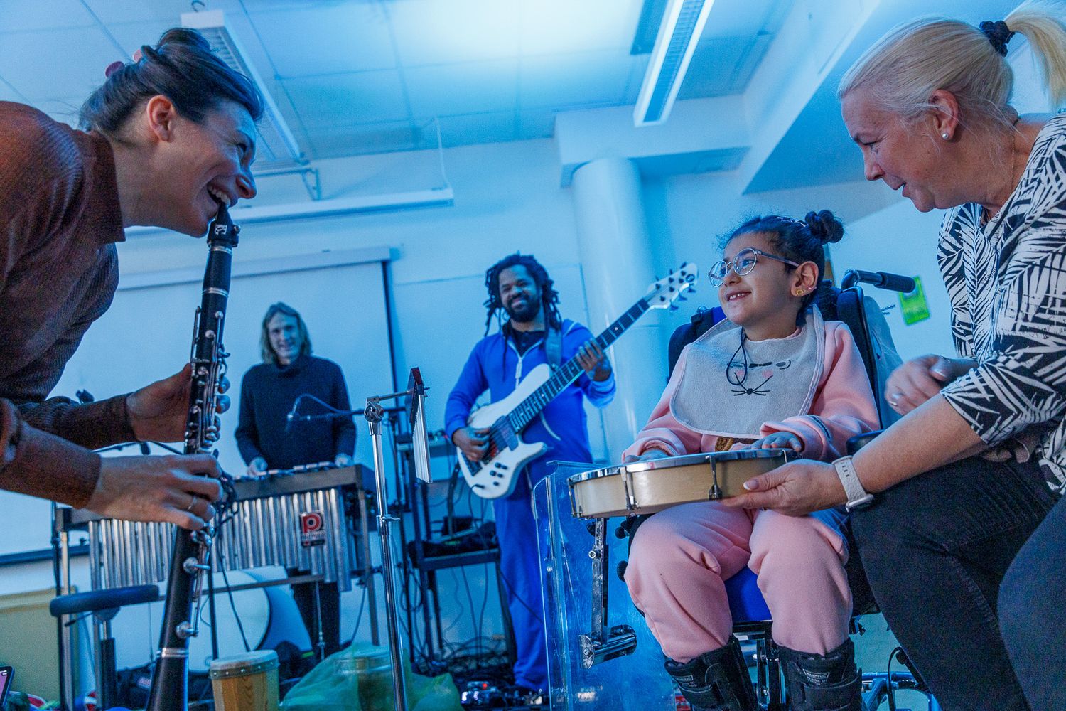 Musicians perform together in a room with blue lighting during a live session.