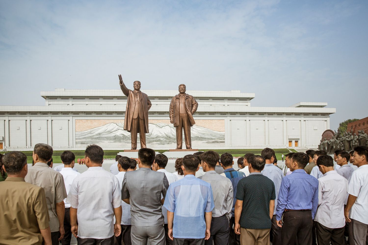 Large crowd gathered in front of monumental statues at a North Korean memorial site.