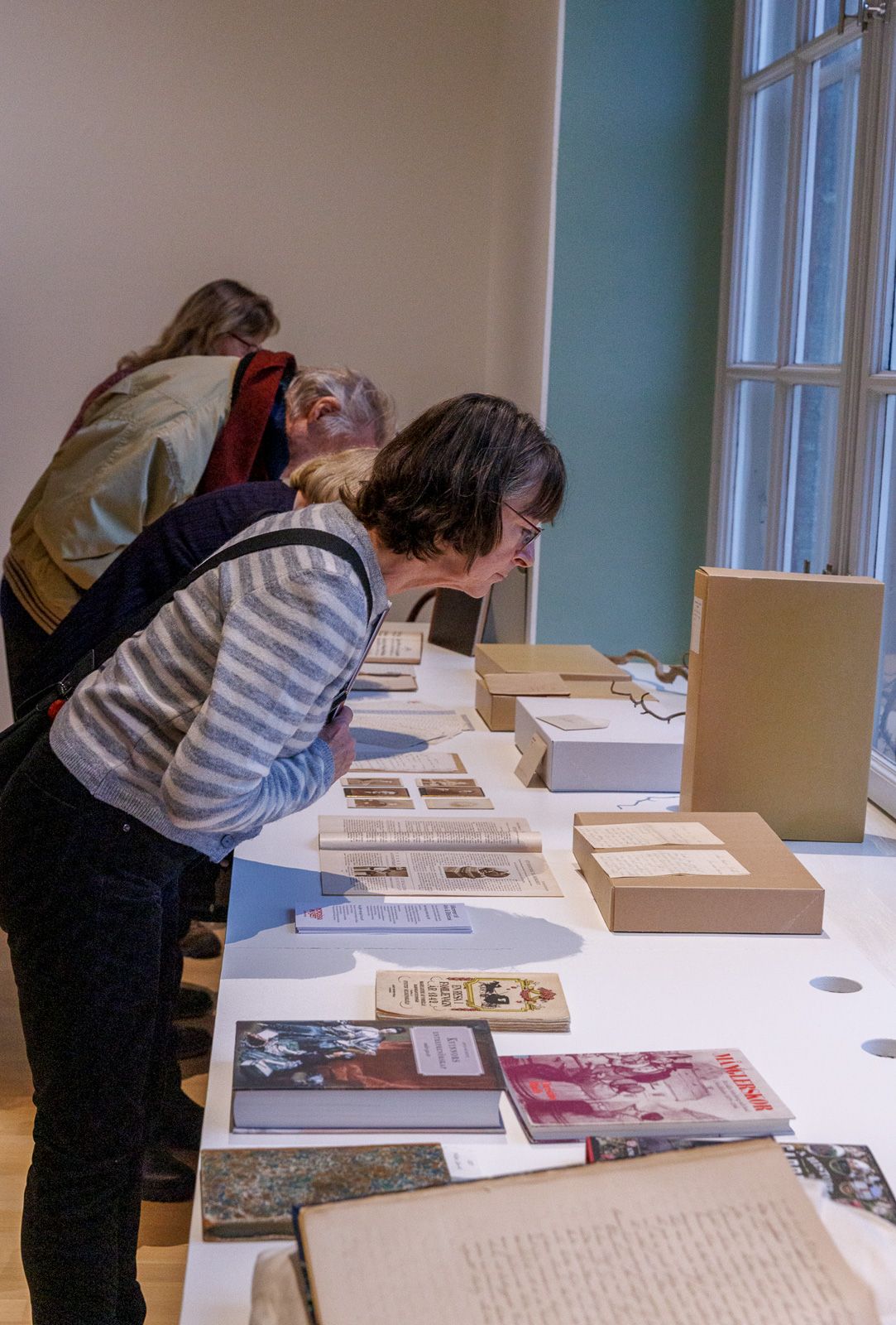 People examining documents and materials displayed on a white table.