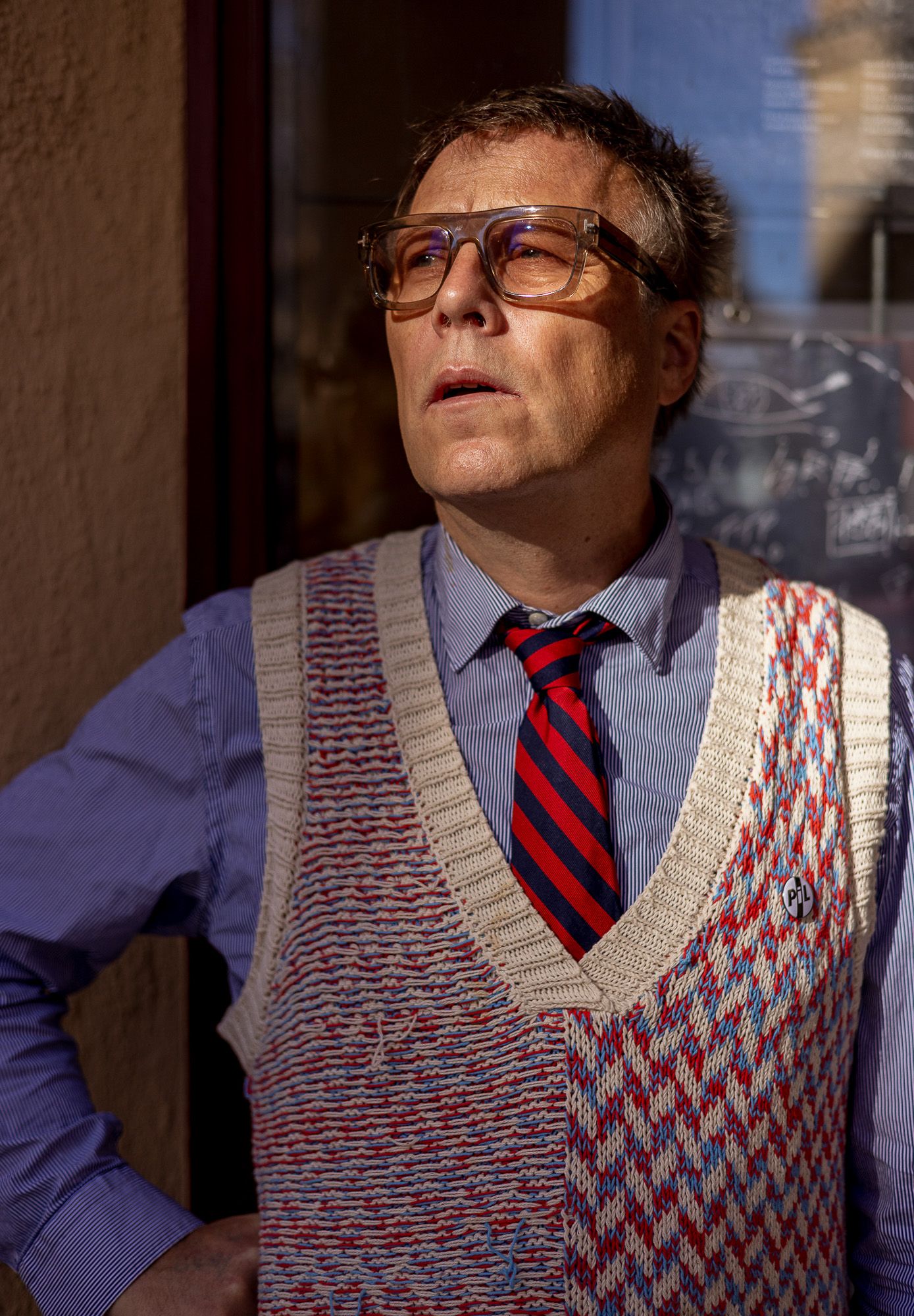 Person wearing patterned sweater vest and striped tie in dramatic lighting.