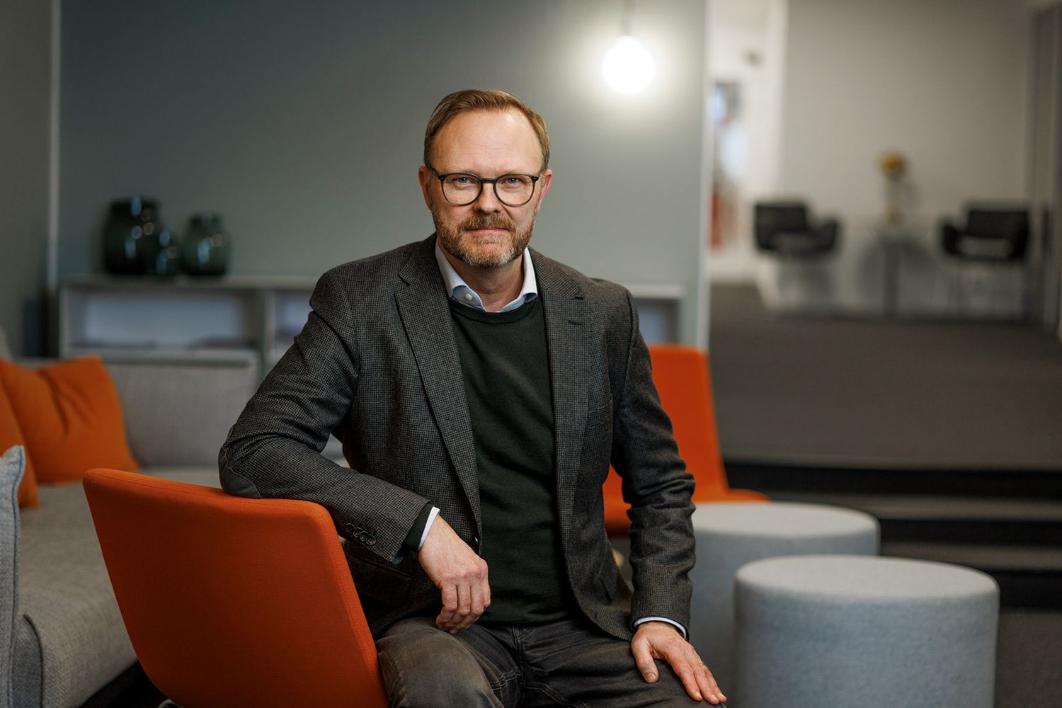 Professionellt kontorsporträtt som visar person sittande i orange stol mot en grå vägg