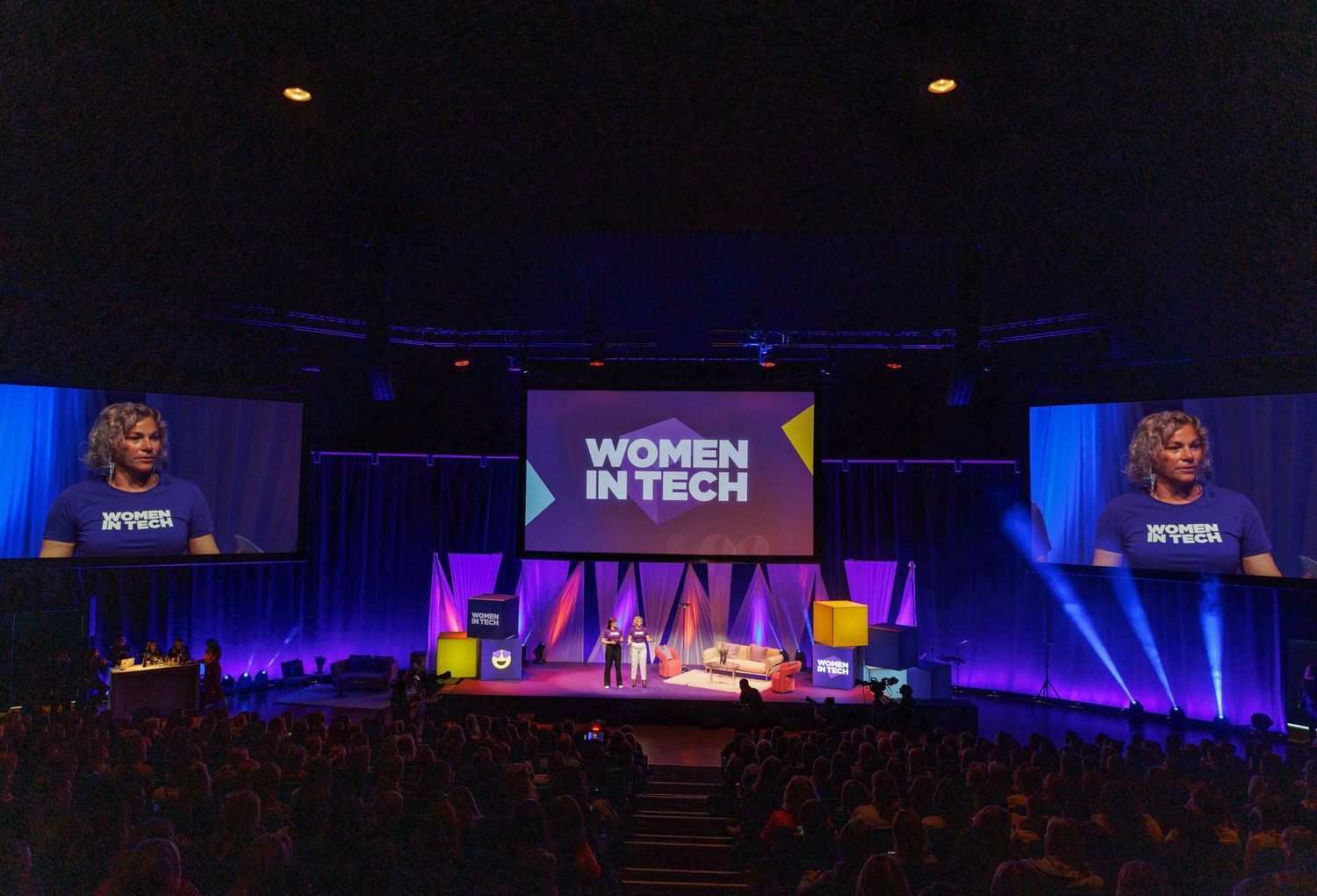 Wide view of conference auditorium with blue lighting and illuminated stage.