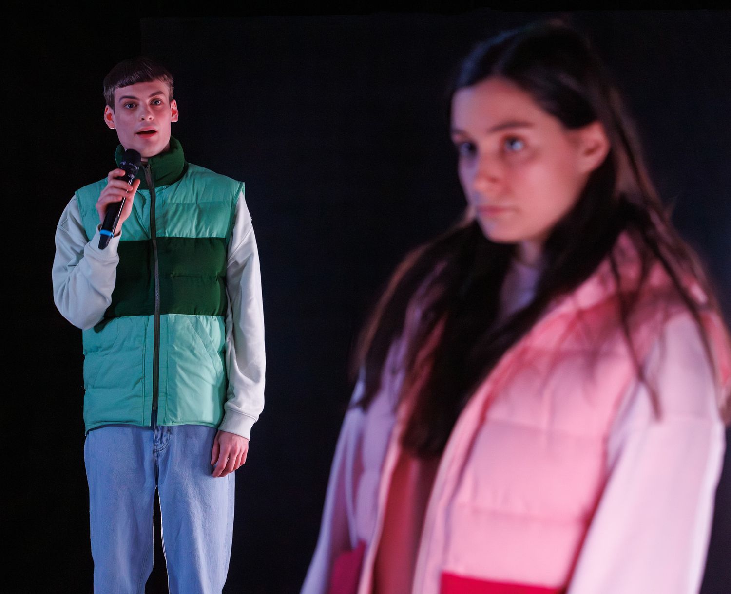 Two performers in contrasting outfits standing against dark background with dramatic lighting.