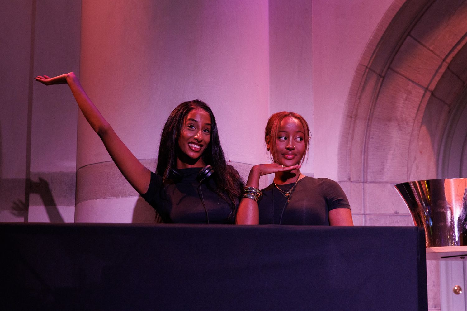 DJs performing at a nightclub under pink and purple lighting.