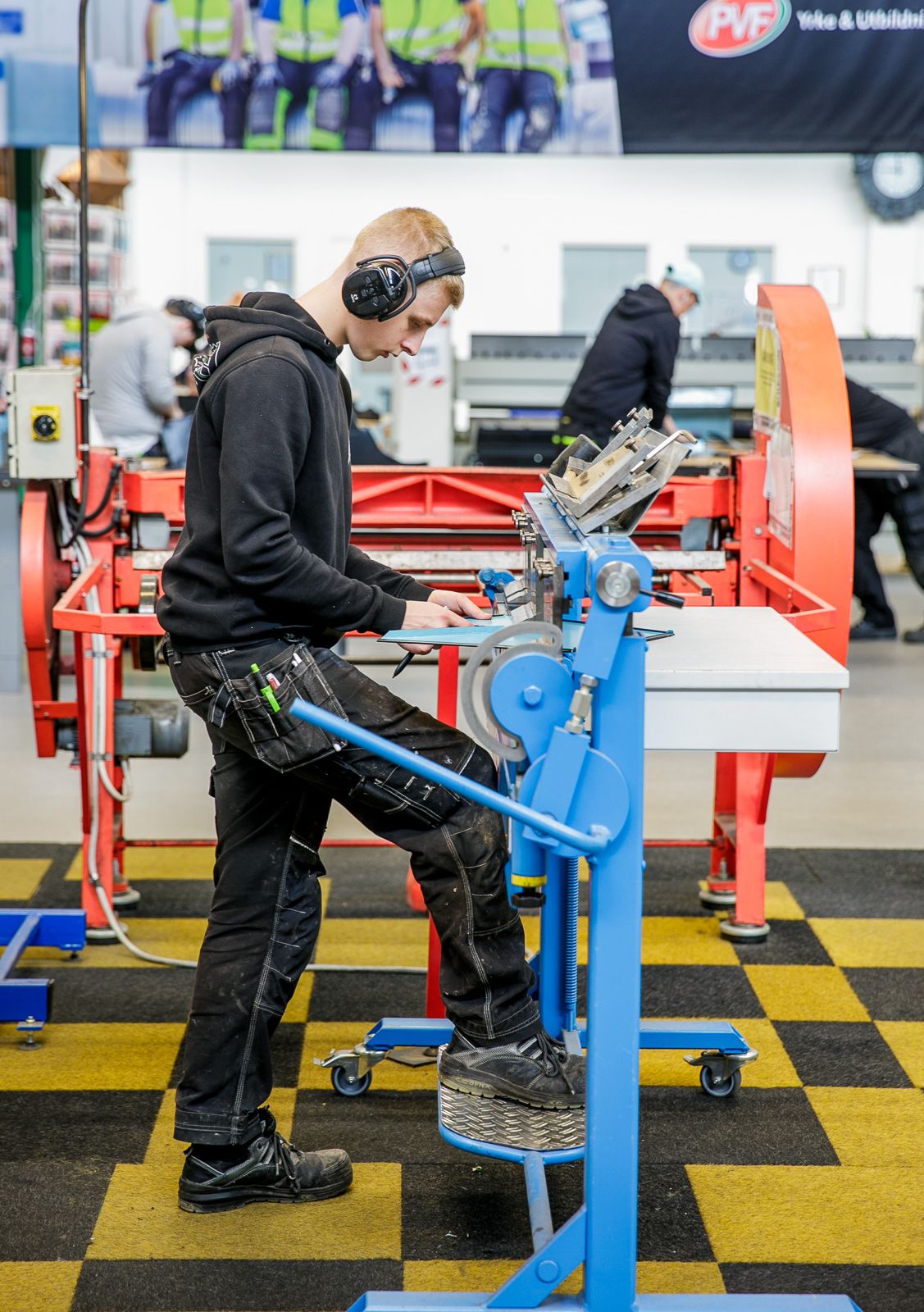 Person operating industrial machinery while wearing protective headphones in workshop setting.