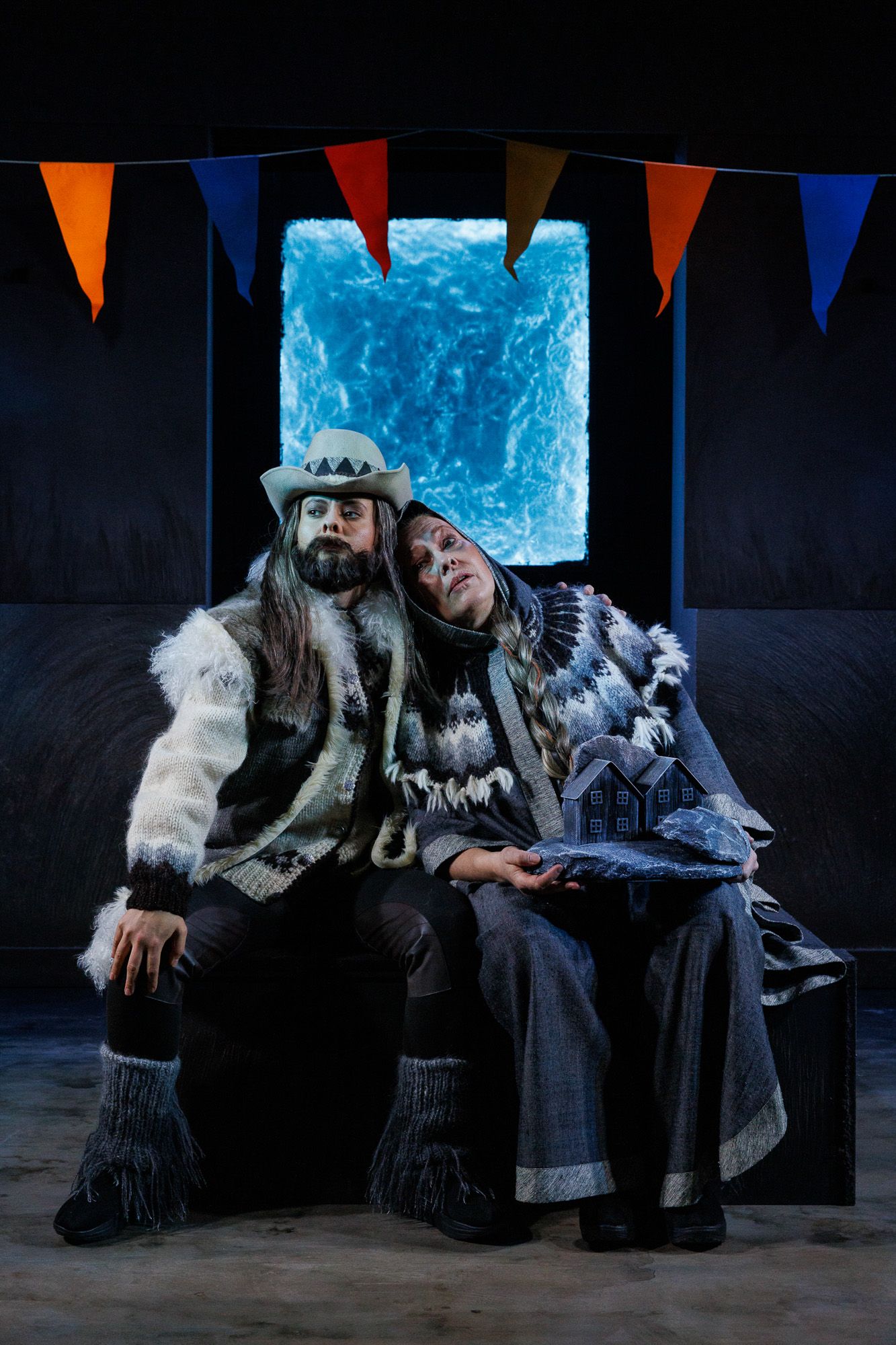 Stage scene with blue backdrop and colorful pennants featuring performers in winter costumes.