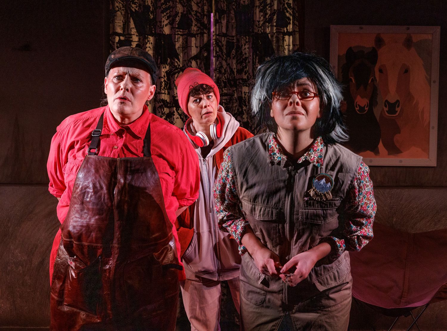 Theater performers in red and dark clothing on dimly lit stage.