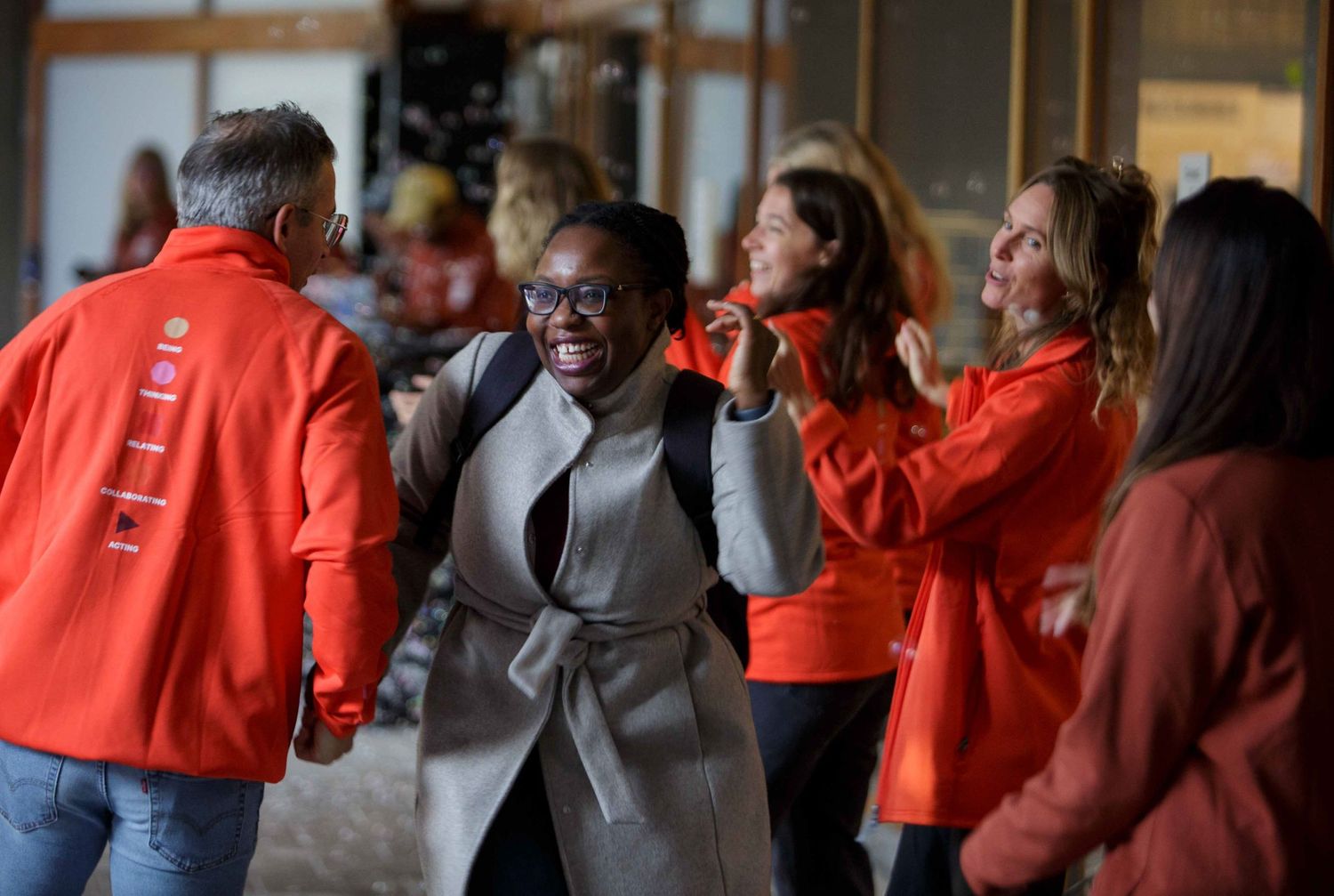 A crowd of people wearing red and orange jackets gathered in a hallway or corridor.