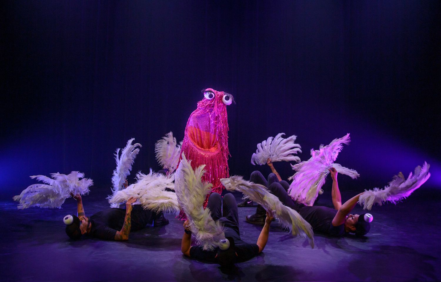 Theatrical performance featuring dancers in pink costumes lying on a dark stage.