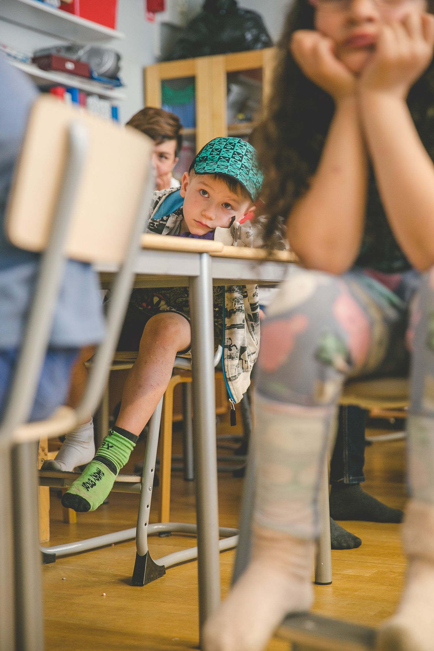 Children's feet hanging from chairs in a classroom with wooden floors.