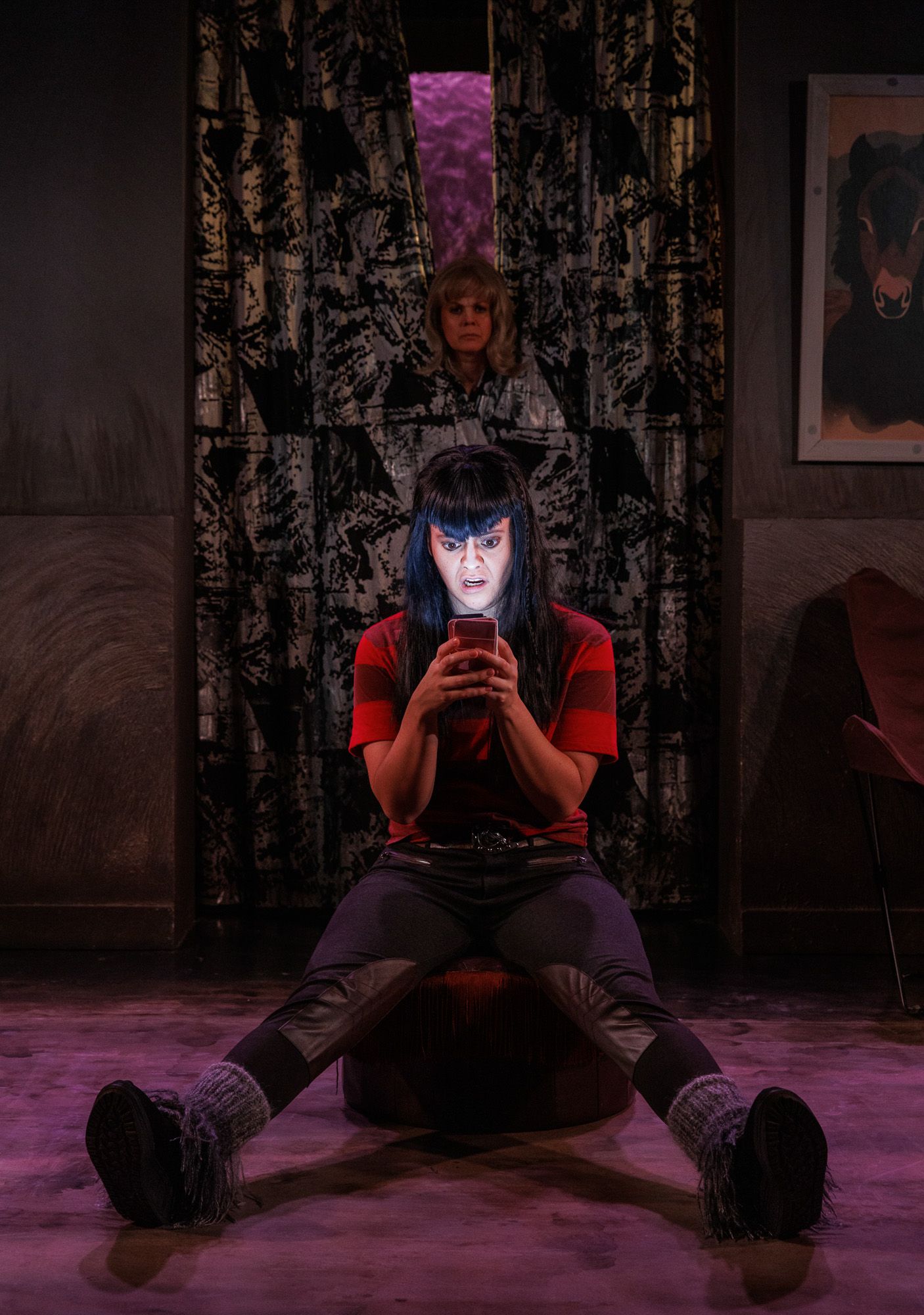 Dramatic scene on stage with moody purple lighting and patterned backdrop.